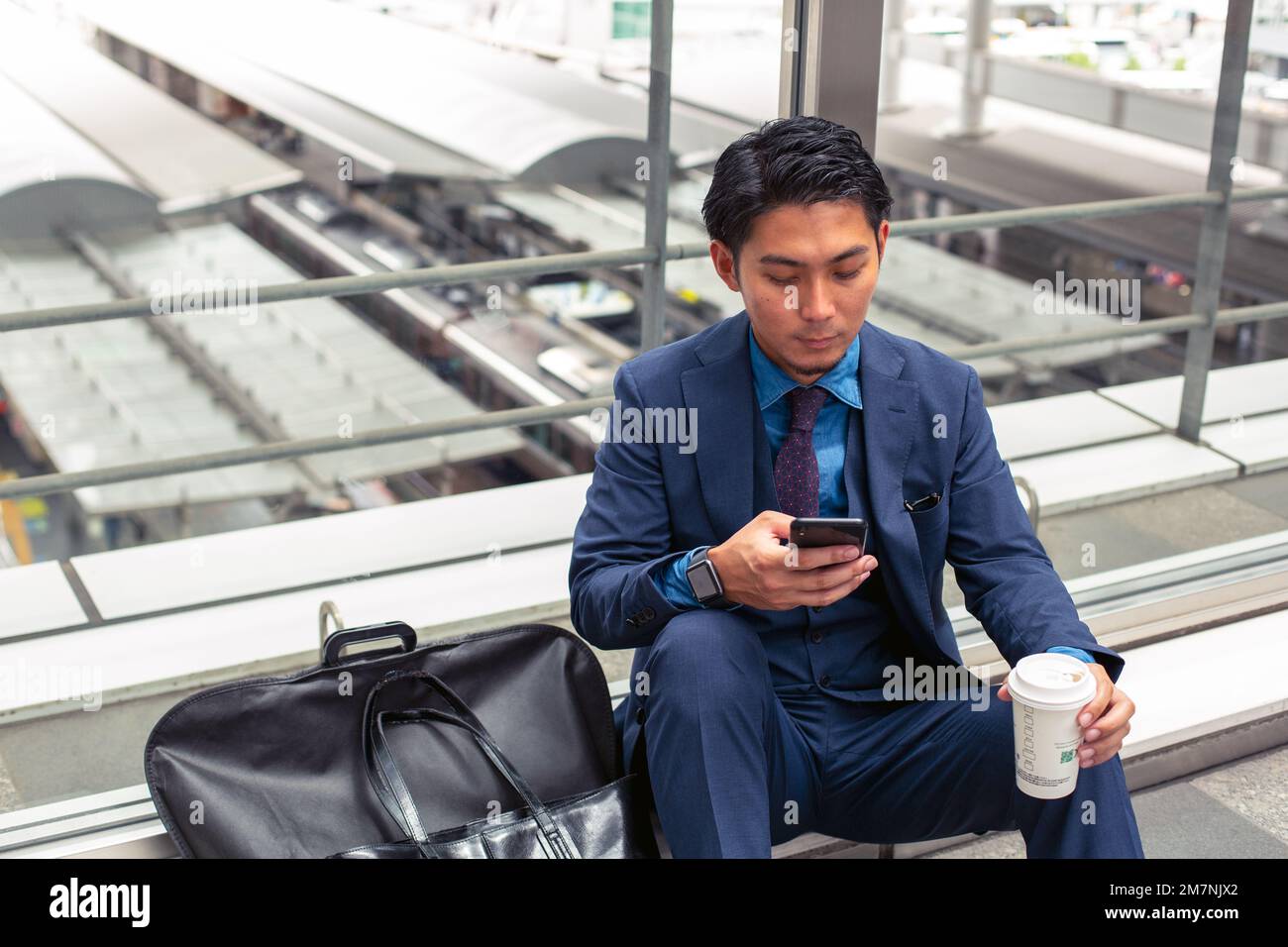 A young businessman in a blue suit in a city, looking at his mobile phone screen, texting or reading a message. Stock Photo