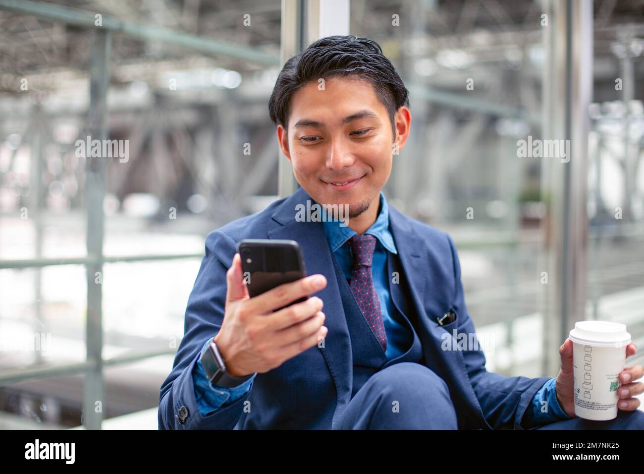 A young businessman in a blue suit in a city, looking at his mobile phone screen, texting or reading a message. Stock Photo