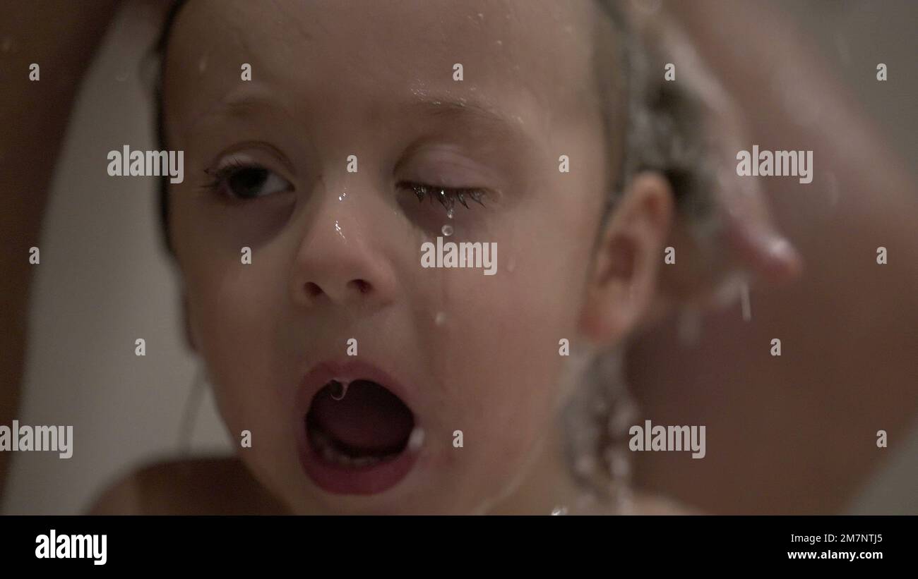 Crying baby washing hair in shower, shampoo itchy eyes in bath. Upset child cries Stock Photo