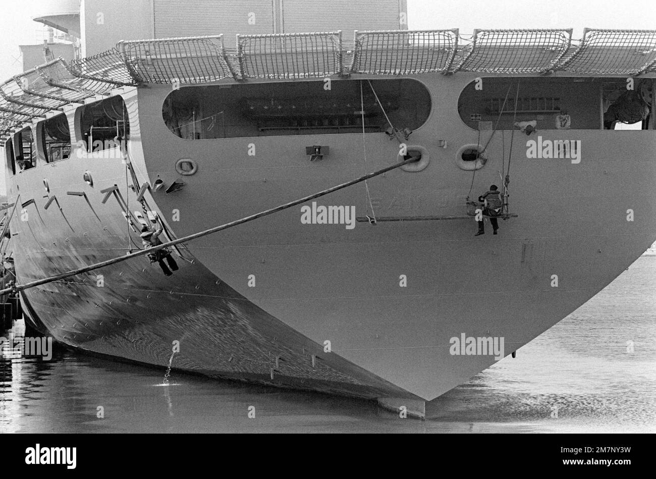 A crewman repaints the name on the stern of the combat stores ship USS SAN JOSE (AFS 7). Base: Naval Station, Subic Bay State: Luzon Country: Philippines (PHL) Stock Photo