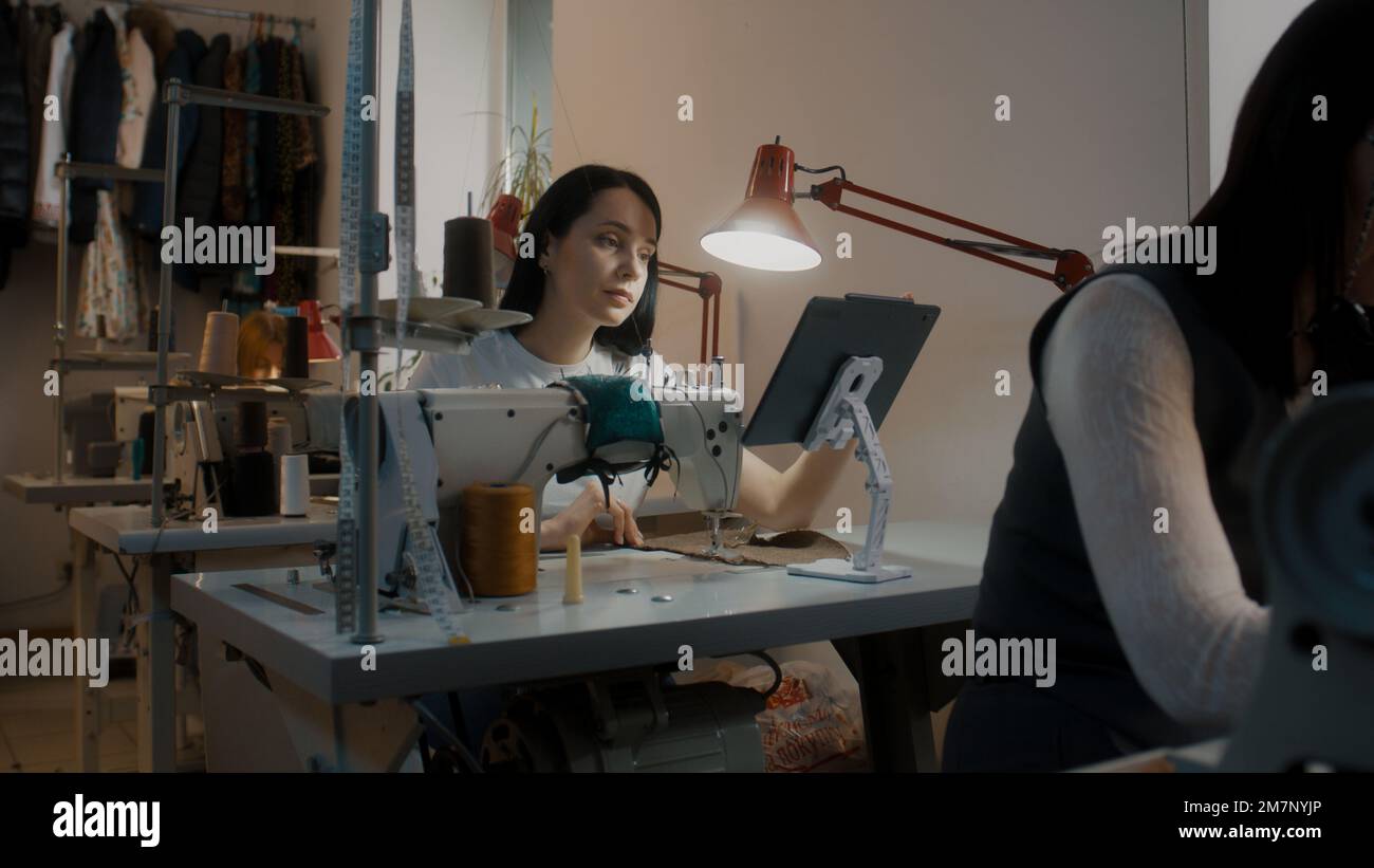Sewing Machine Tablet Female fashion designer or dressmaker touches tablet, sits at sewing ...