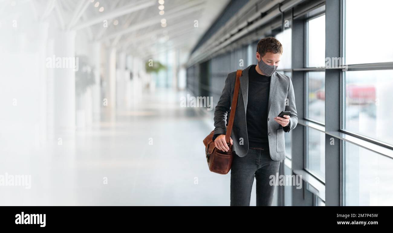 Travel business man wearing coronavirus face mask walking in airport using vaccine passport mobile phone app. Business travel professional people Stock Photo