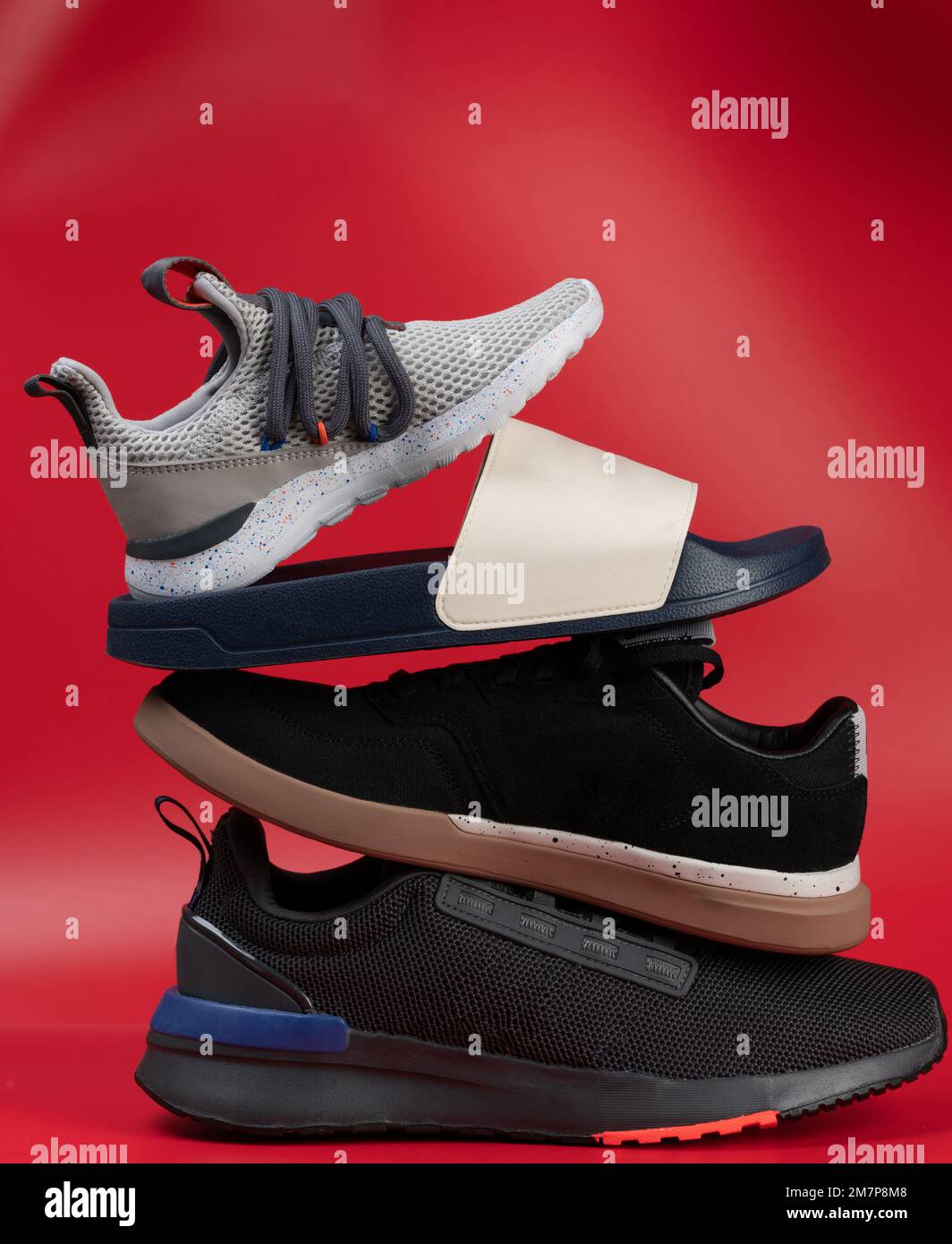 Group of sport and casual new shoes ontop of each other in stack isolatedon red studio background Stock Photo