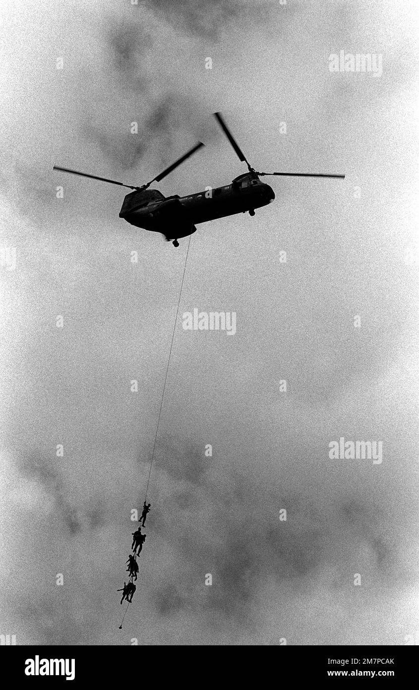 A right side view of an in-flight Army CH-47 Chinook helicopter during Open House demonstration. Army rappelling team members hang from the helicopter as they circle the flightline area. Base: Hickam Air Force Base State: Hawaii (HI) Country: United States Of America (USA) Stock Photo