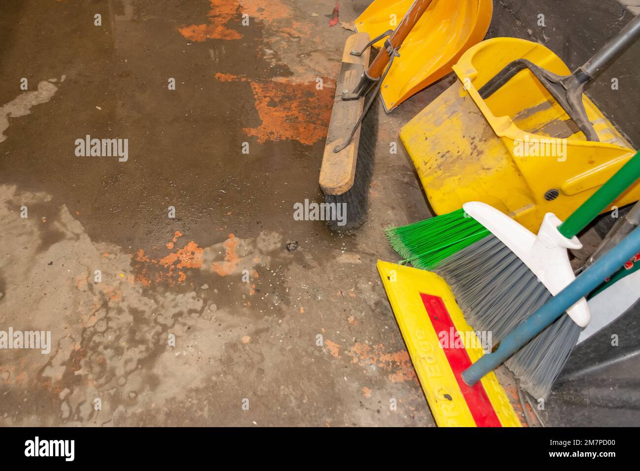 brooms and dustpan on a pile of cleaning materials on a wet cement floor in a garage Stock Photo