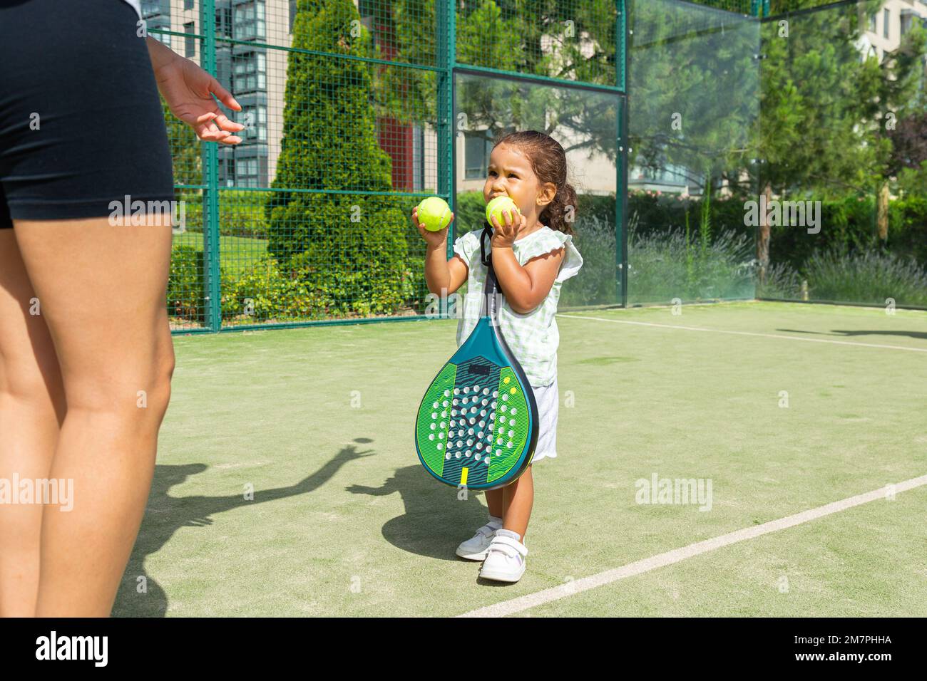 Little girl handing tennis balls to her mother on a padel tennis court Stock Photo