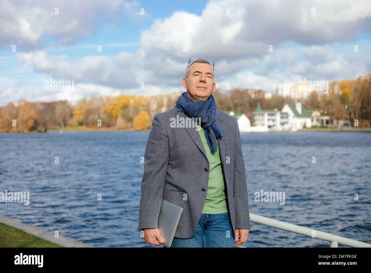 Old businessman in stylish clothes enjoying with closed eyes natural beauty. Man walk outdoors near water pond.  Stock Photo
