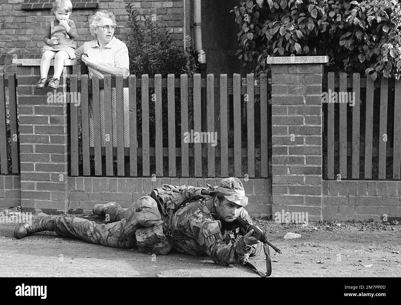 An old woman and a child watch as a member of U.S. Air Force 317th Combat Control Team aims his