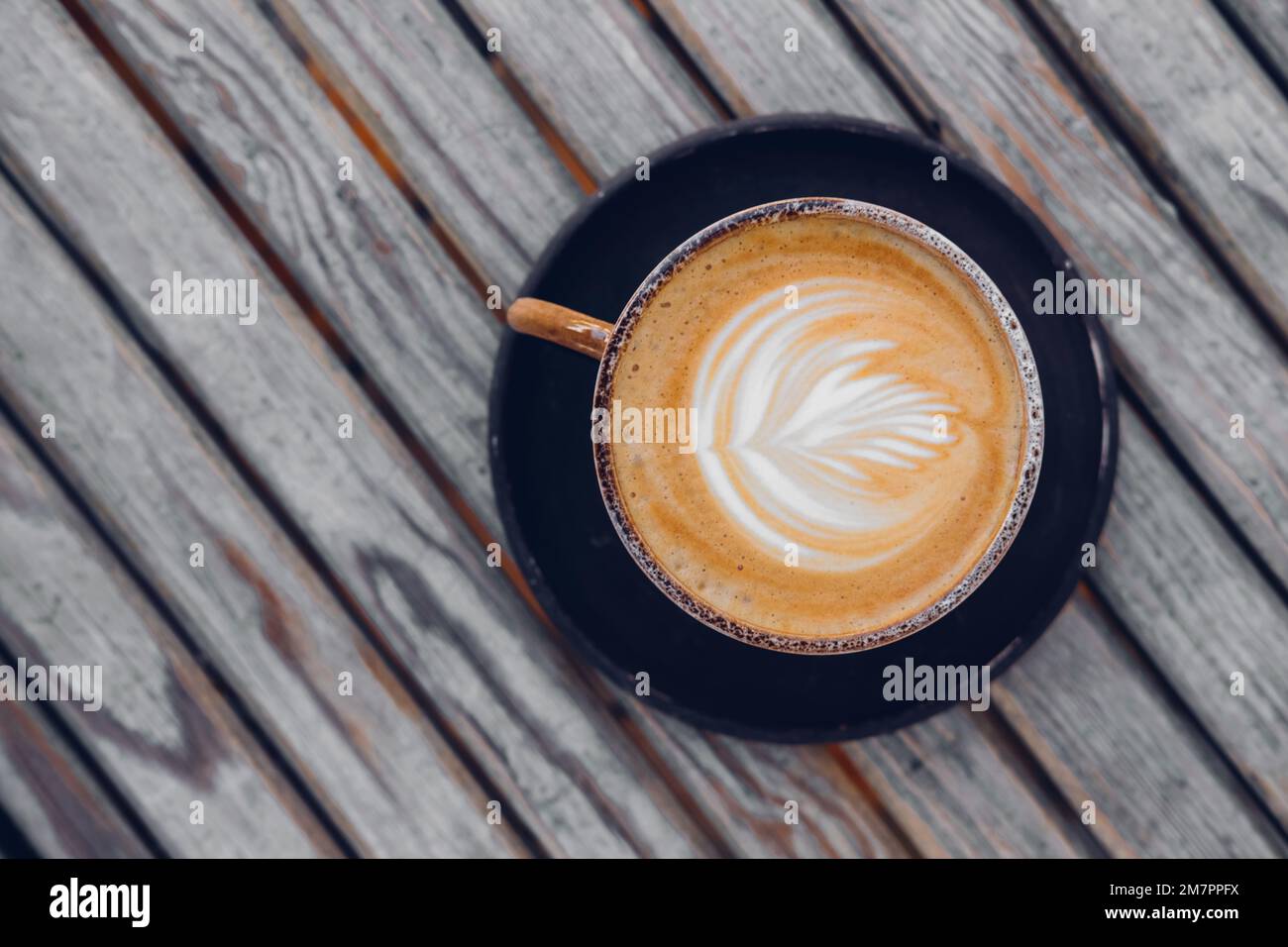 https://c8.alamy.com/comp/2M7PPFX/top-view-on-stylish-latte-coffee-mug-with-flower-art-on-wooden-table-background-2M7PPFX.jpg