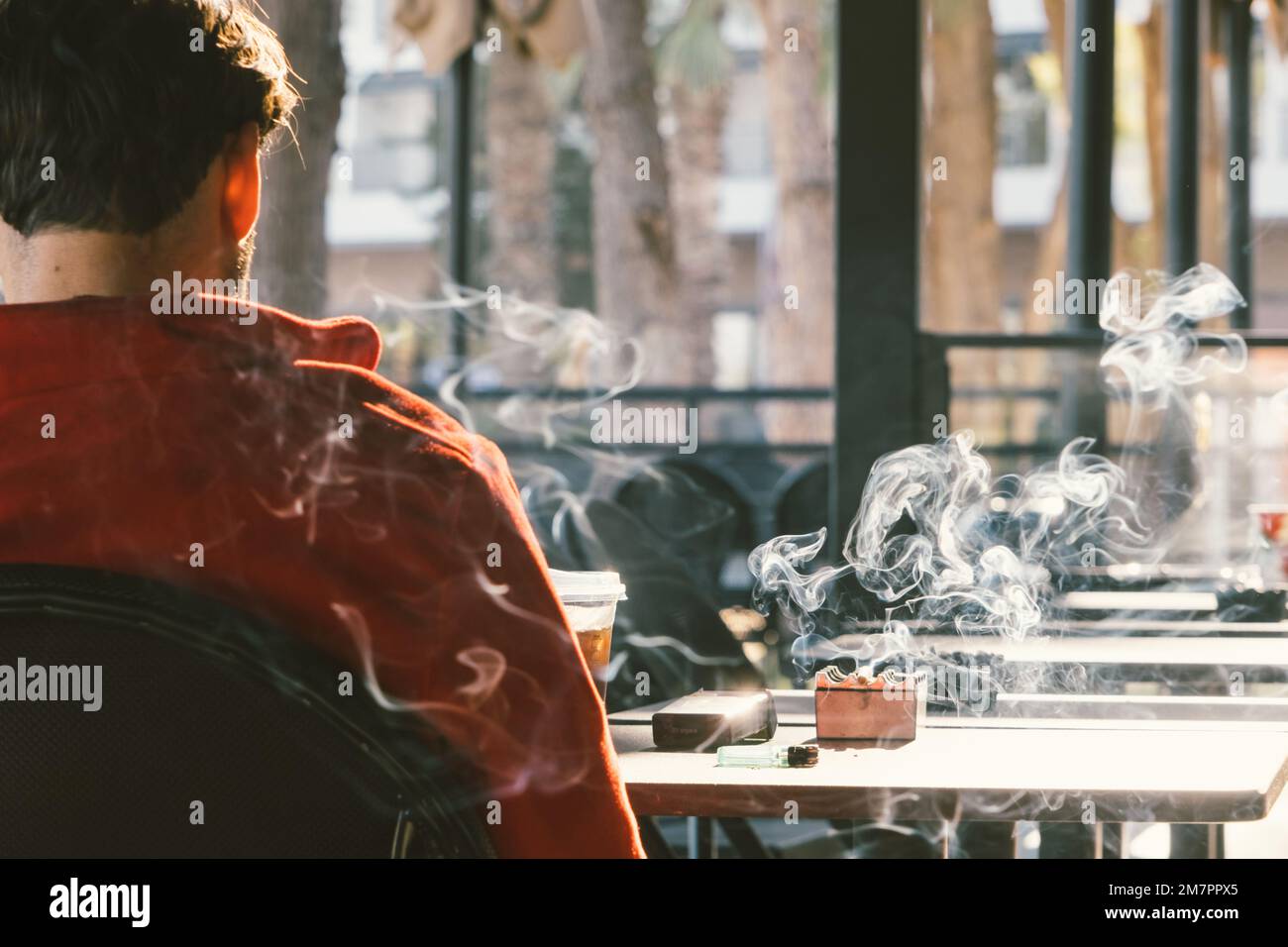 Back view of man smoking tobacco cigarette in cafe. Unhealthy lifestyle