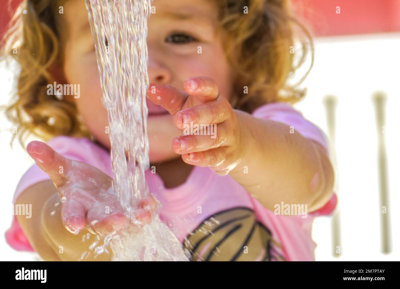 Young girl stands in front of water streeming from faucet washing her hands. Stock Photo