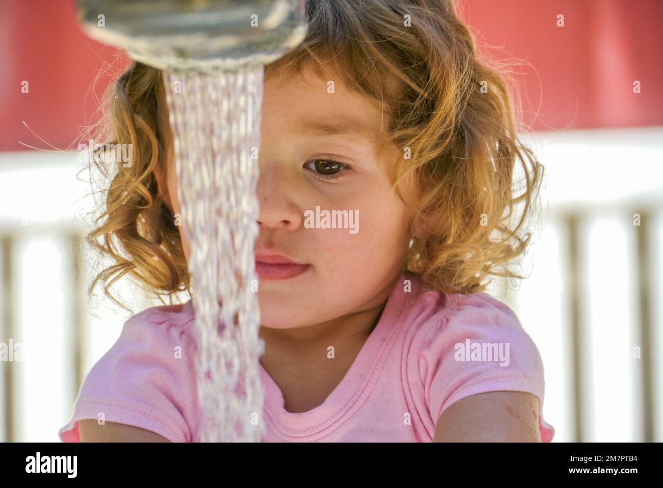 Young girl stands in front of water streaming from faucet washing her hands. Stock Photo
