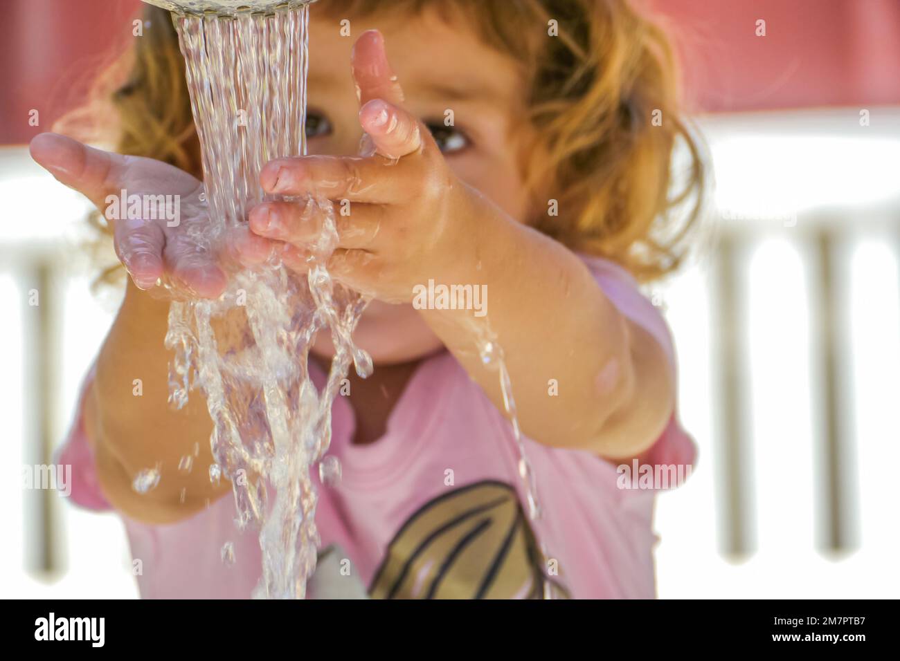 Young girl stands in front of water streaming from faucet washing her hands. Stock Photo