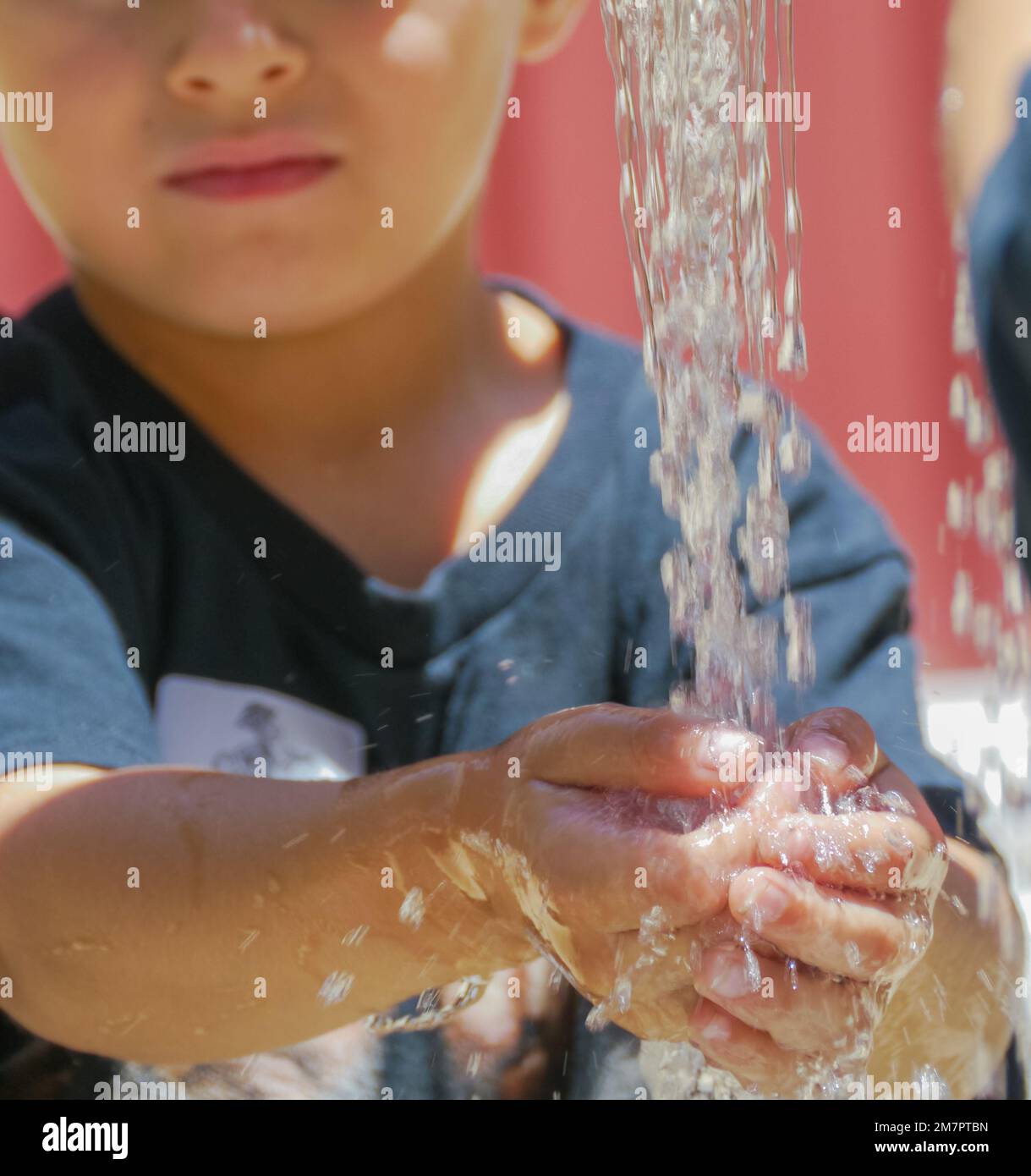 Young child boy male stands in front of water streaming from faucet washing his hands. Stock Photo