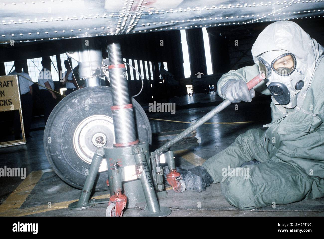 A ground crewman in protective clothing jacks up an H-53 Sea Stallion helicopter to check the tires during a chemical warfare training exercise. Base: Kirtland Air Force Base State: New Mexico (NM) Country: United States Of America (USA) Stock Photo