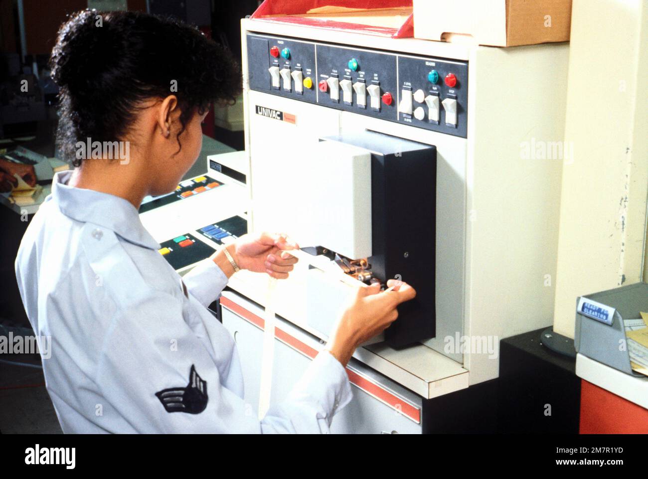 An operator checks a punched tape from a Univac tape reader in the computer side of the message center. The airman is a member of the 1965th Communications Squadron, Air Force Communications Command (AFCC). Base: Norton Air Force Base State: California (CA) Country: United States Of America (USA) Stock Photo