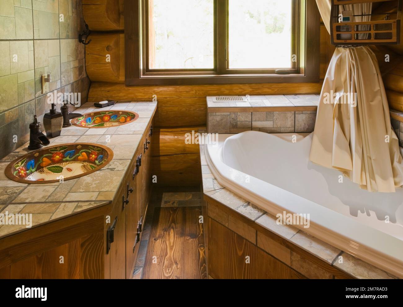 Ceramic tile countertop inlaid with hand painted copper sinks and bathtub in main bathroom inside handcrafted red cedar log home. Stock Photo