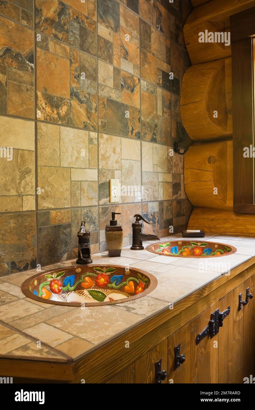 Ceramic tile countertop inlaid with hand painted copper sinks in main bathroom inside handcrafted red cedar log home. Stock Photo