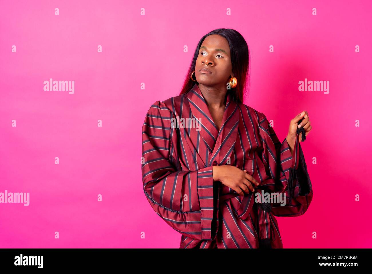Black ethnic man in a studio, LGTBI concept, wearing a red kimono and a long wig Stock Photo