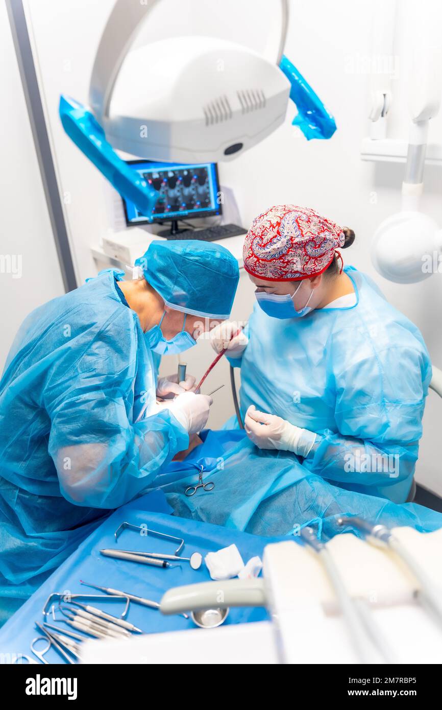 Dental clinic, dentist doctor and the assistant with blue suits performing an operation of an implant Stock Photo