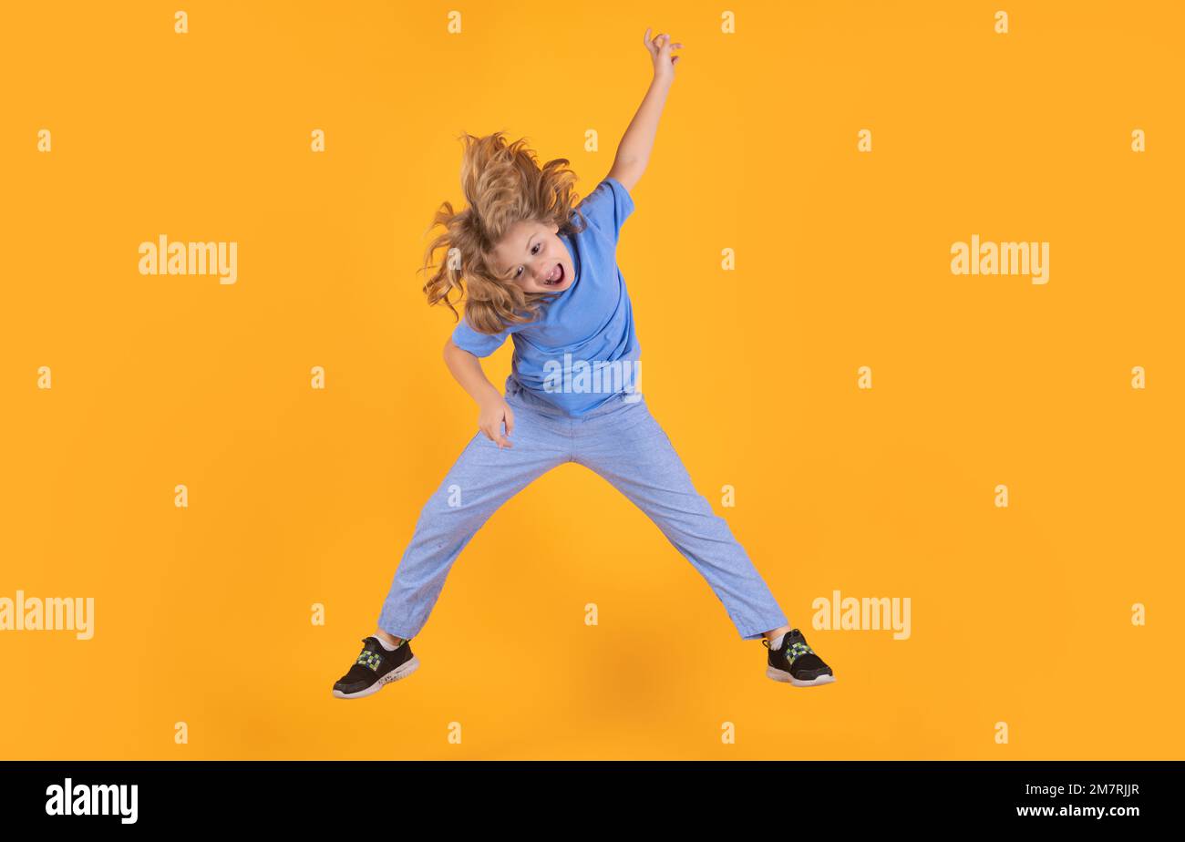Funny boy jumping in air. Kid boy jump fly movement wear shirt and jeans isolated on yellow studio background. Stock Photo