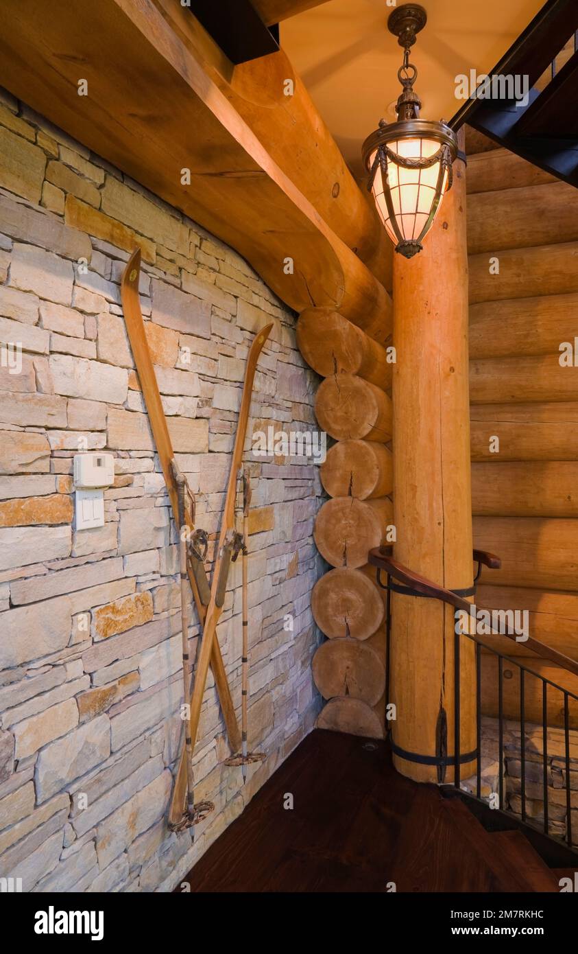 Old wooden skis on natural stone wall next to stairs leading to basement inside luxurious Scandinavian style log home. Stock Photo