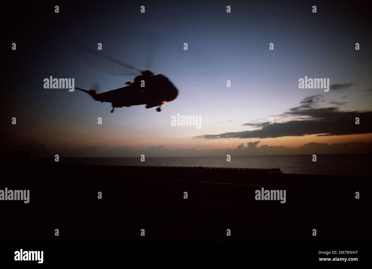A silhouetted view of an SH-3 Sea King helicopter hovering above the aircraft carrier USS AMERICA (CV 66). Country: Mediterranean Sea (MED) Stock Photo