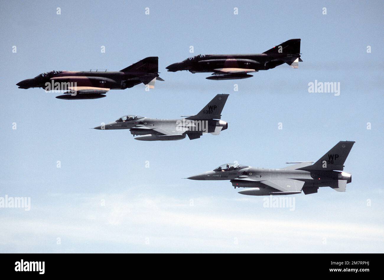 An air-to-air left side view of two F-16 Fighting Falcon aircraft being escorted by two F-4 Phantom II aircraft (above), to their new command with the 8th Tactical Fighter Wing. Base: Kunsan Air Base Country: Republic Of Korea (KOR) Stock Photo