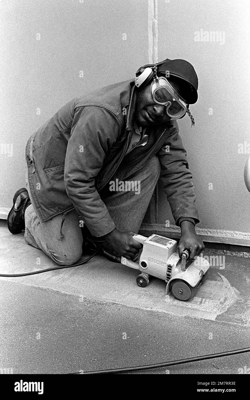 SEAMAN Ted Mitchell uses a deck grinder to remove old paint from the