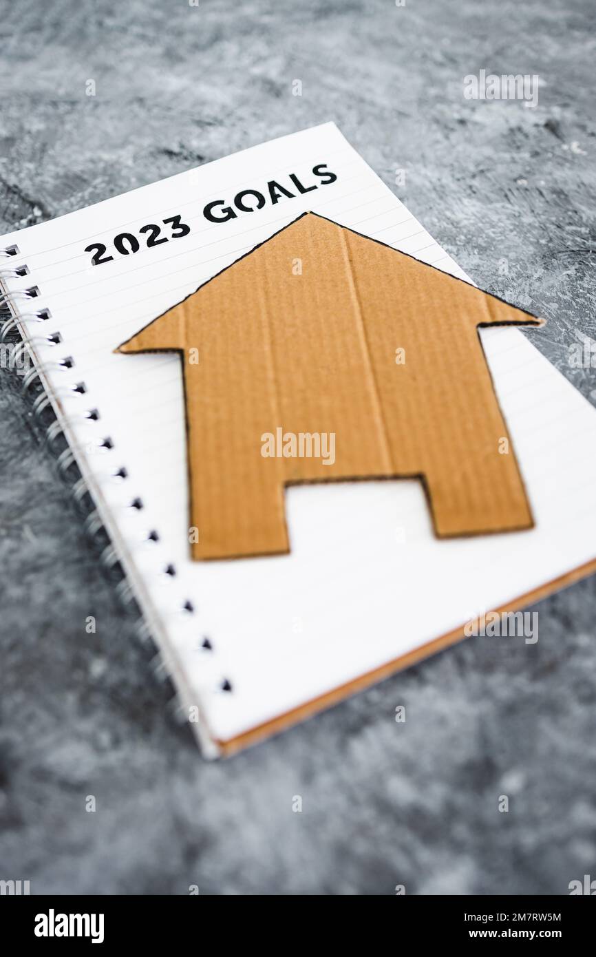 concept of buying a house or settling down, 2023 goals on notebook with cardboard house Stock Photo