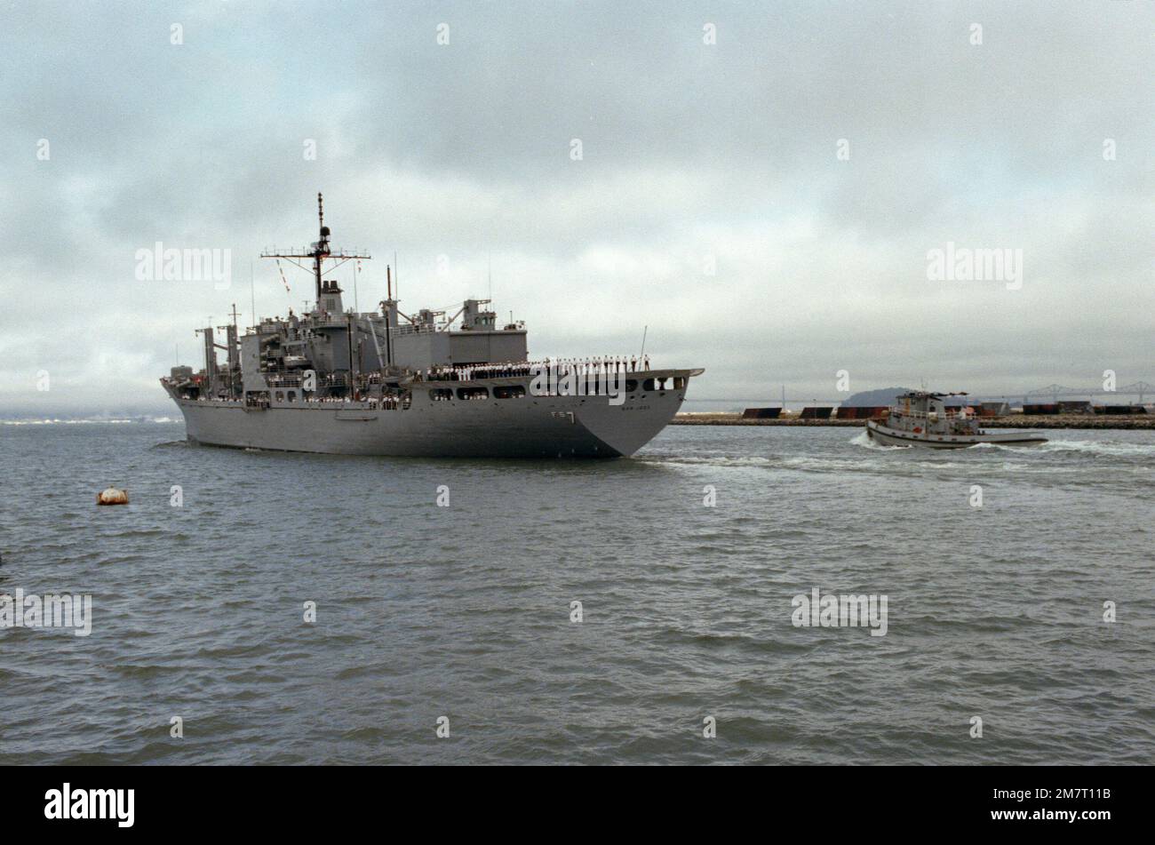 Crew members man the rails of the Mars-class combat store ship USS SAN JOSE (AFS 7) as it leaves Alameda, California, for its new home port in Guam. Country: Unknown Stock Photo