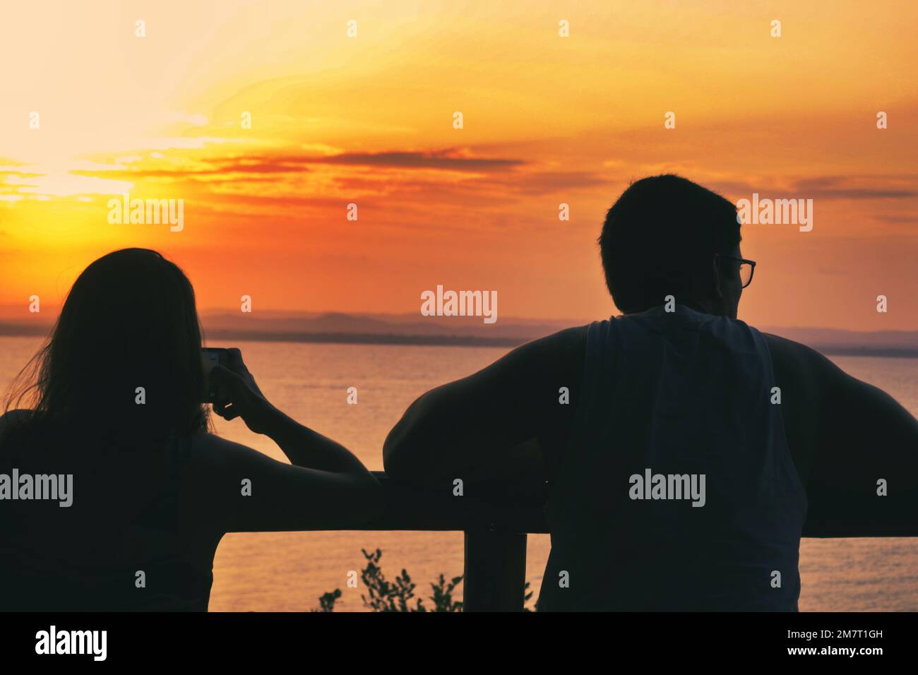 A couple watches the sunset. They are together, but they look apart Stock Photo