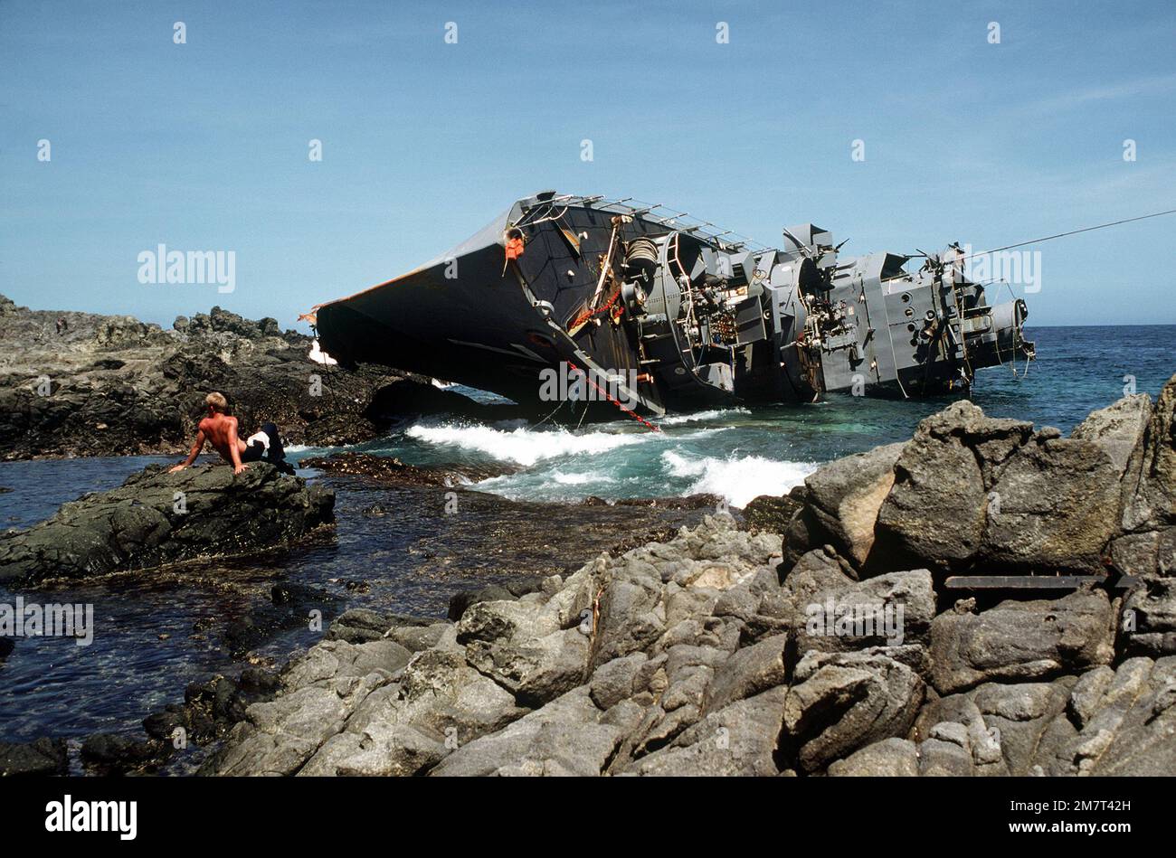 A view of the capsized Philippine destroyer DATU KALANTIAW (ex-USS BOOTH DE-170). In the foreground, a crewman from the ammunition ship USS MOUNT HOOD (AE-29) takes a break from salvage operations. Base: Calayan Island Country: Philippines Stock Photo