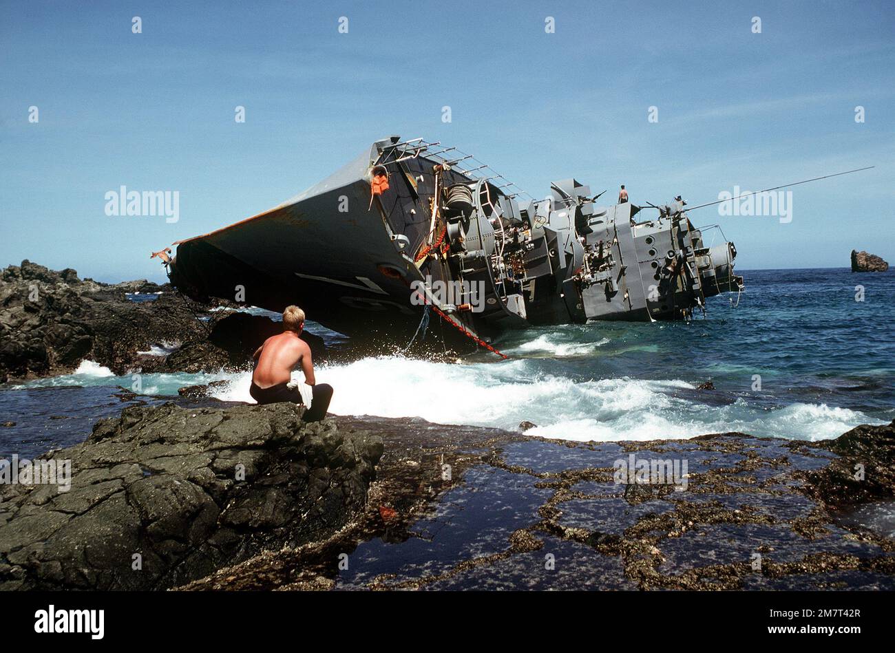 A view of the capsized Philippine destroyer DATU KALANTIAW (ex-USS BOOTH DE-170). In the foreground, a crewman from the ammunition ship USS MOUNT HOOD (AE-29) takes a break from salvage operations. Base: Calayan Island Country: Philippines Stock Photo