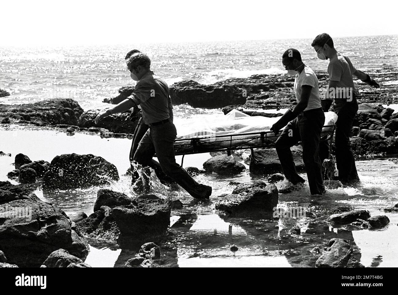 Four crewmen from the ammunition ship USS MOUNT HOOD (AE-29) carry a body over rocks during search and rescue (SAR) operations for the beached and overturned Filipino frigate RPS DATU KALANTIAW (PS-76). The frigate was overtaken by Typhoon Clara. Base: Calayan Island Country: Philippines Stock Photo