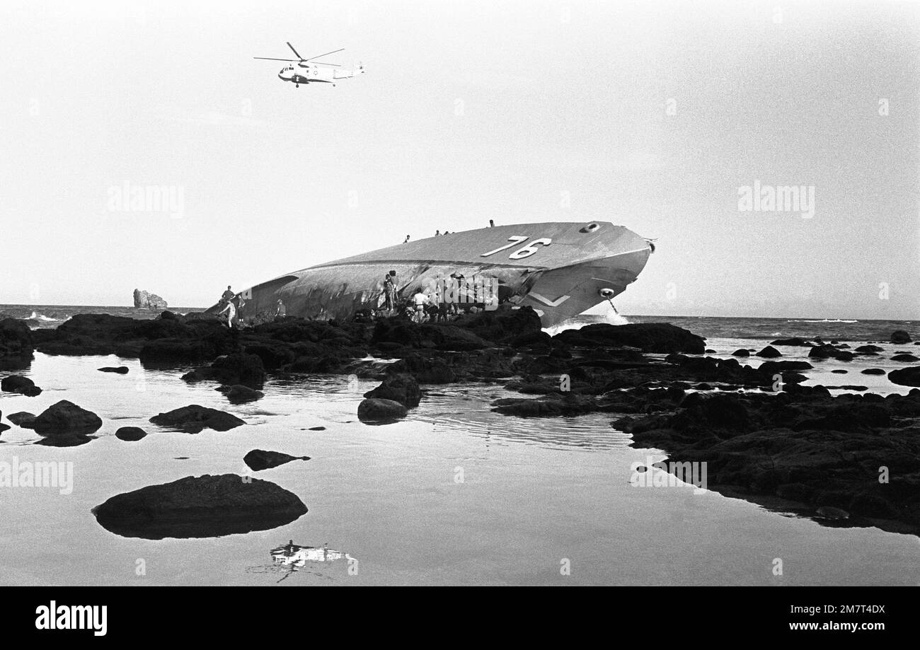 Crewmen from the ammunition ship USS MOUNT HOOD (AE-29) participate in search and rescue (SAR) operations as they work from the rocks near the beached and overturned Filipino frigate RPS DATU KALANTIAW (PS-76). The frigate was overtaken by Typhoon Clara. Base: Calayan Island Country: Philippines Stock Photo