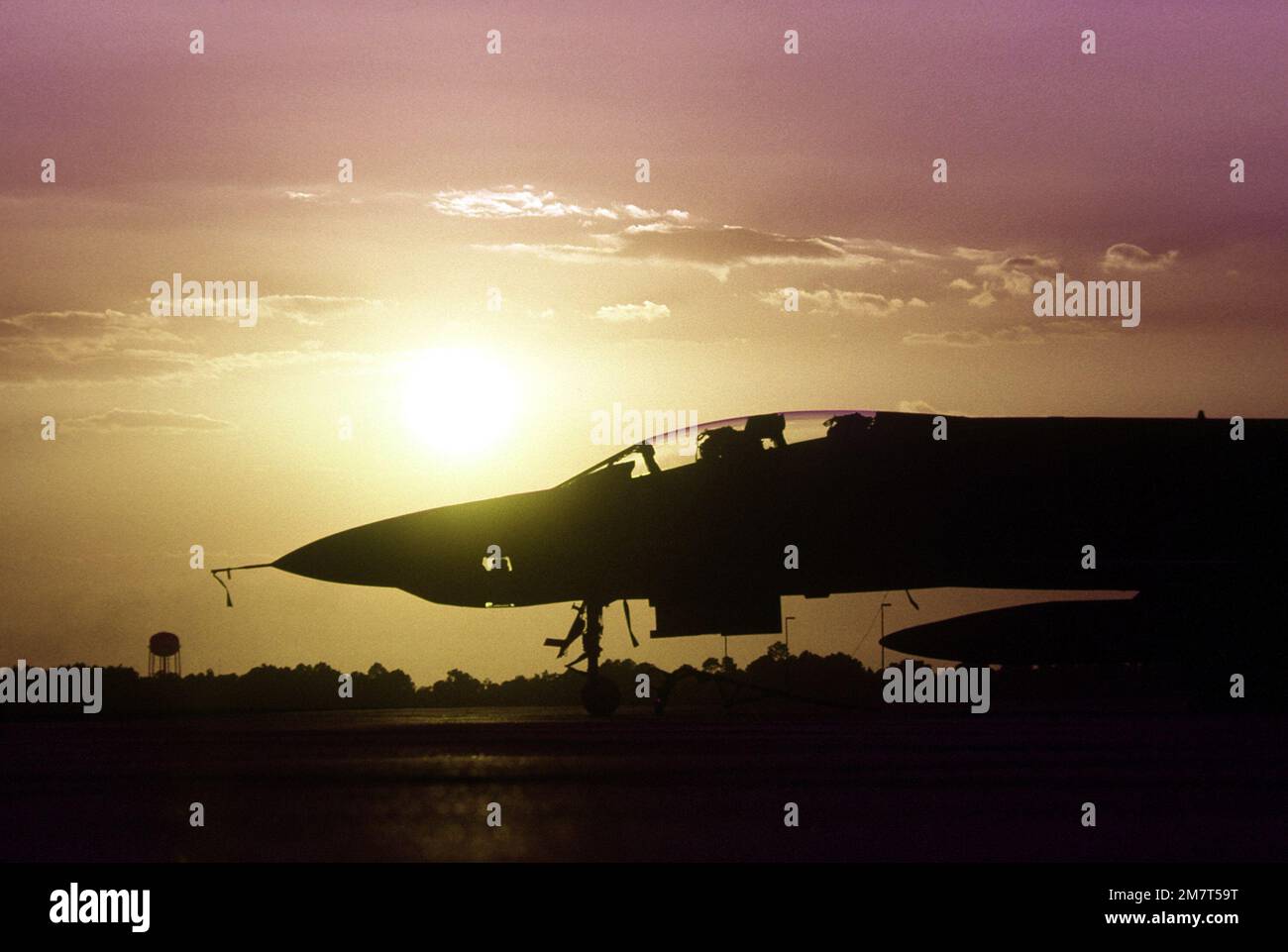 An F-4E Phantom II aircraft is silhouetted against the orange sky while parked on the flight line during exercise PHOTO Finish '81. Subject Operation/Series: PHOTO FINISH '81 Base: Gulfport State: Mississippi (MS) Country: United States Of America (USA) Stock Photo