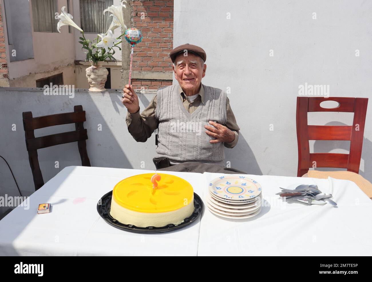 Senior man celebrating his birthday at family house. Blowing out candle and holding a balloon. Stock Photo