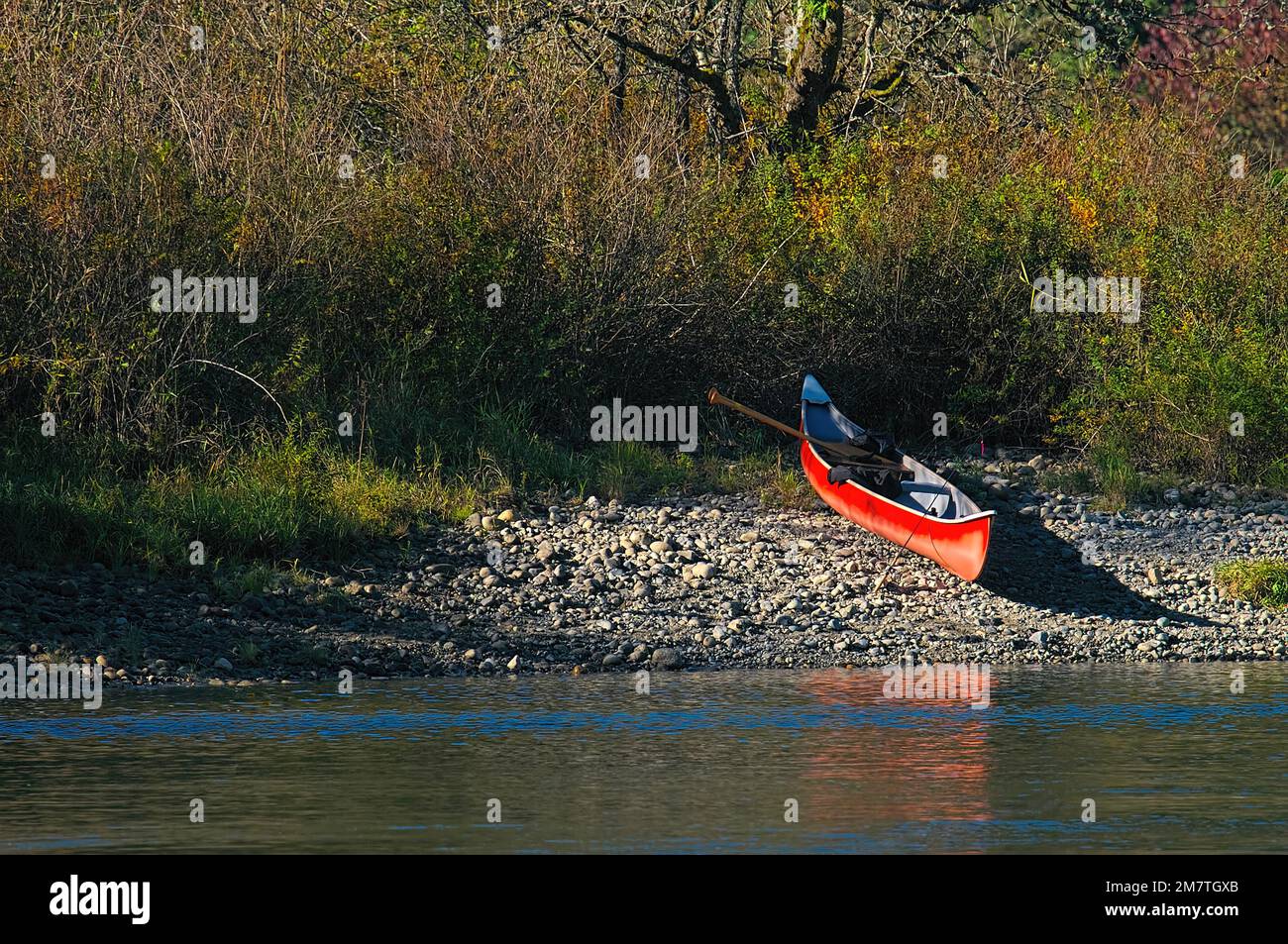 Red canoe on a rocky shore with paddles and fishing rod.  Metro Vancouver, British Columbia, Canada. Stock Photo