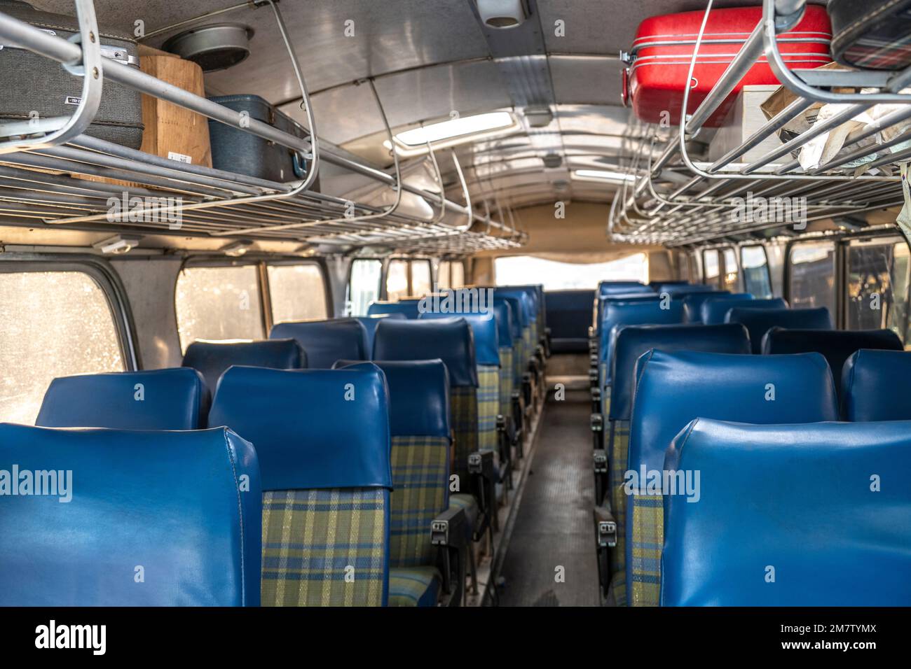 inside a transit bus with blue and pladid seats and luggage rack Stock Photo