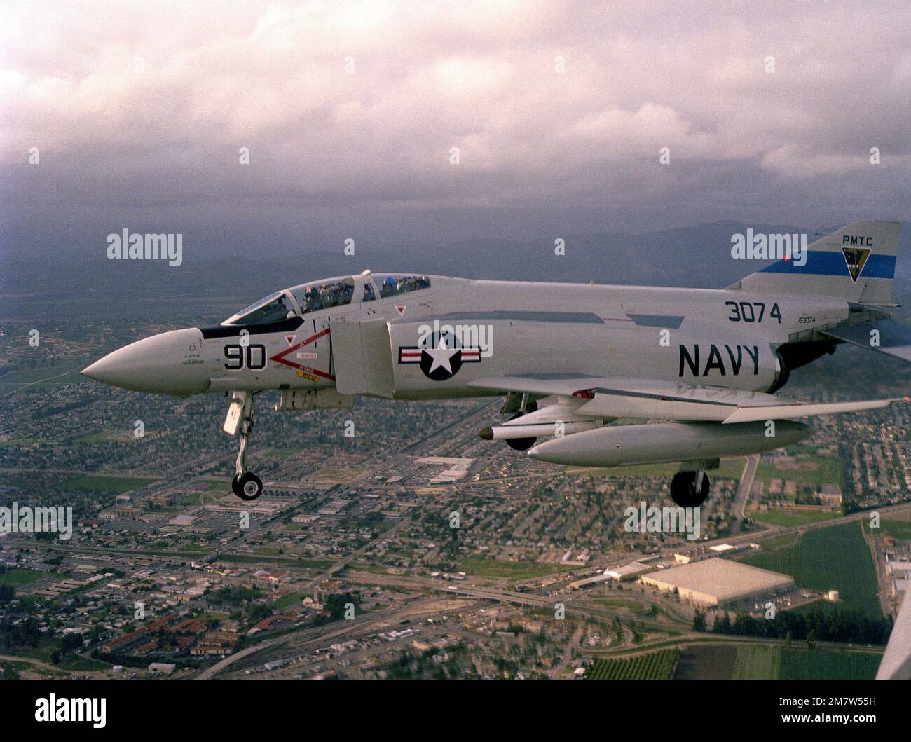 A left side view of an F-4 Phantom II aircraft with advanced medium range air-to-air missiles (AMRAAM) under its wing, in flight over the Pacific Missile Test Center. Base: Naval Air Station, Point Mugu State: California (CA) Country: United States Of America (USA) Stock Photo