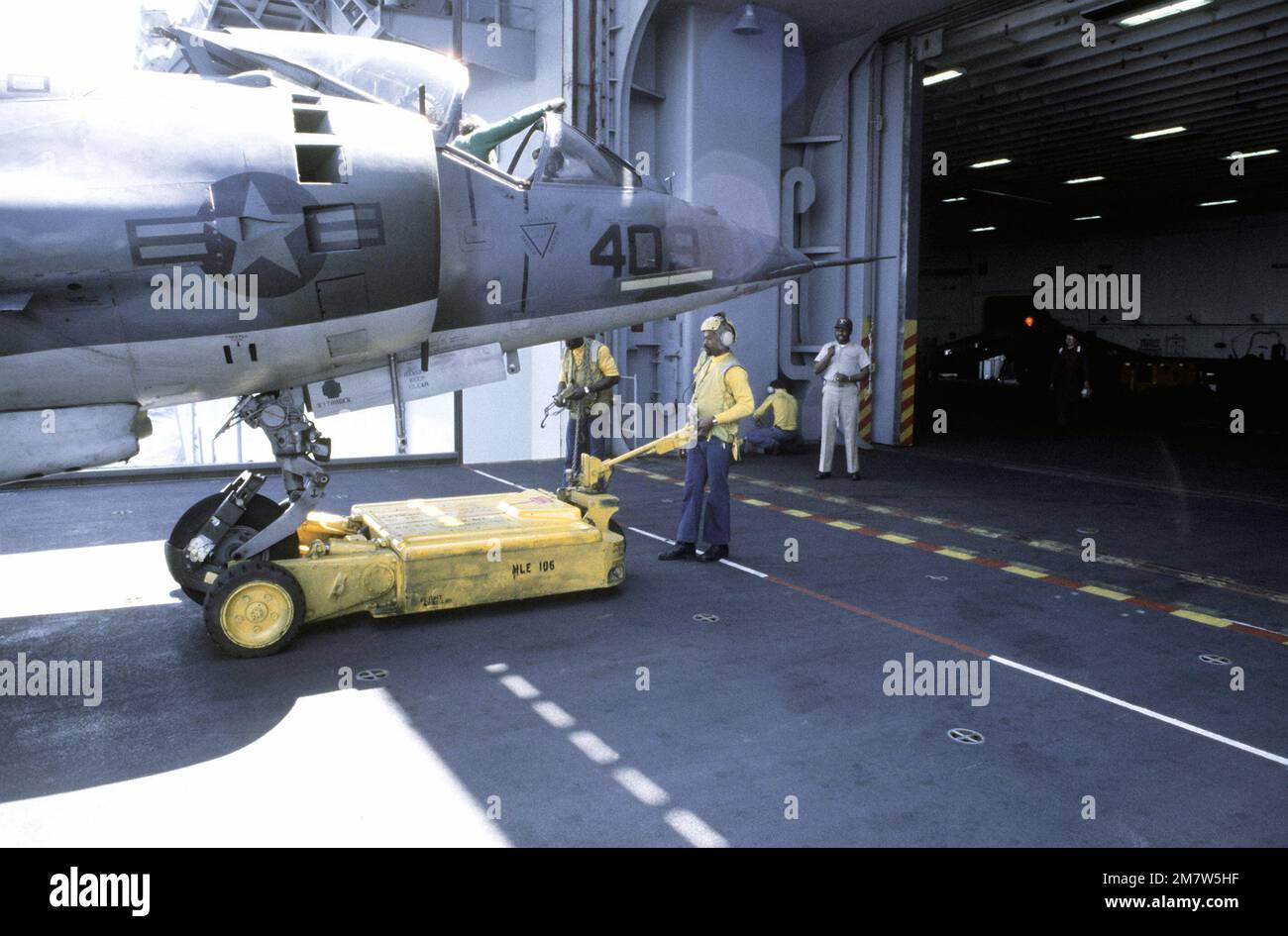 A flight deck crewman maneuvers an AV-8A Harrier aircraft into the hangar with an aircraft spotting hand truck aboard the amphibious assault ship USS NASSAU (LHA-4). Country: Atlantic Ocean (AOC) Stock Photo