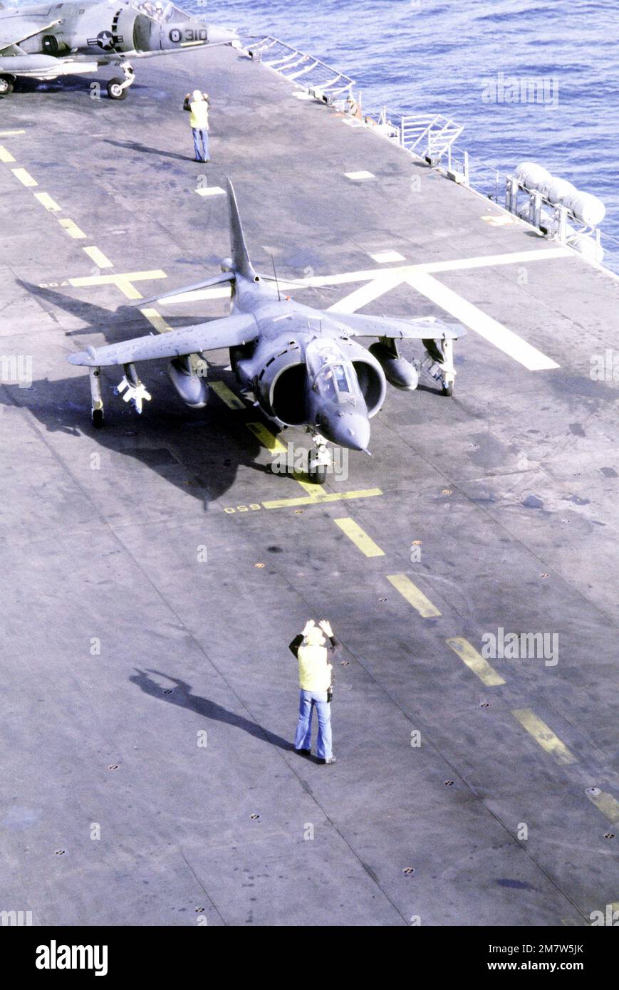 A flight deck crewman signals to the pilot of an AV-8A Harrier aircraft ...