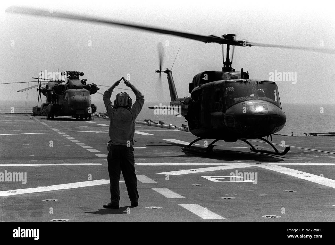 A flight deck crewman signals to a UH1N Iroquois helicopter landing
