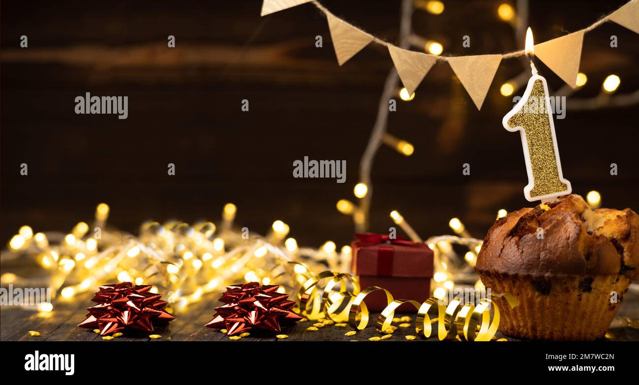 Number 1 gold burning candle in a cupcake against celebration wooden background with lights. Birthday cupcake. Copy space. Banner Stock Photo