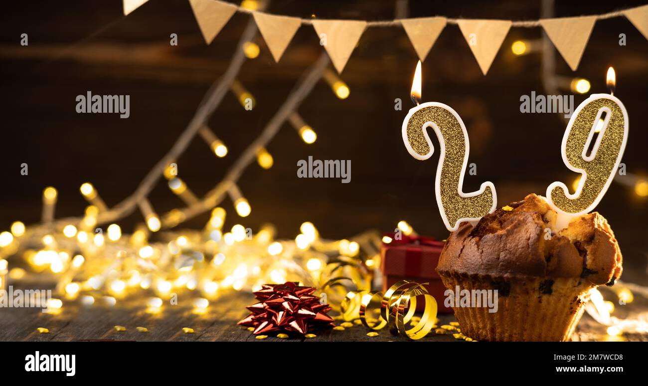 Number 29 gold burning candle in a cupcake against celebration wooden background with lights. Birthday cupcake. Copy space. Banner Stock Photo