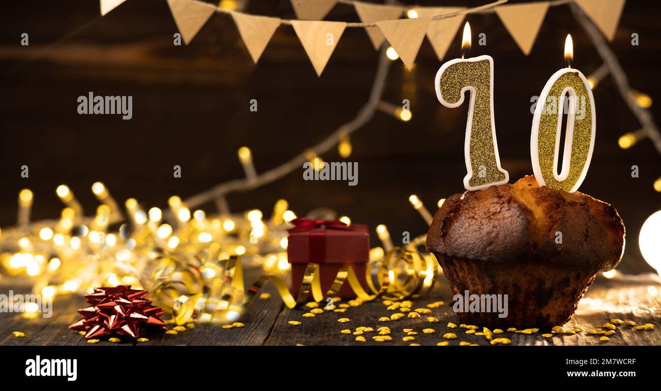Number 70 golden festive burning candles in a cake, wooden holiday background. seventy years of birth. the concept of celebrating a birthday, annivers Stock Photo
