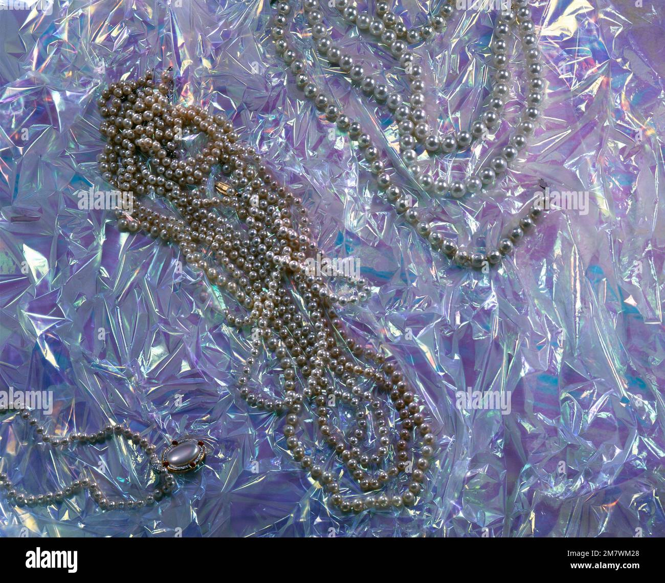 Pearl necklaces on a plastic background with magenta and blue reflections - Collane di perle su fondo di plastica con riflessi magenta e blu. Stock Photo