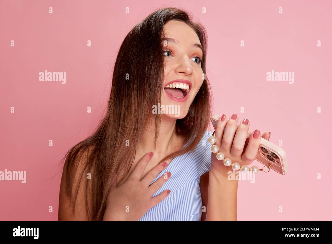 Portrait of young emotive girl posing, emotionally talking on phone over pink studio background. Communication. Concept of emotions, lifestyle, youth Stock Photo