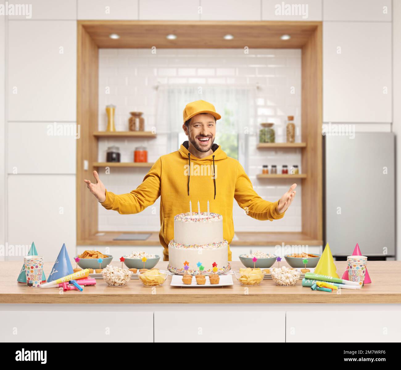 Guy in a kitchen standing behind a counter with cake and party snacks